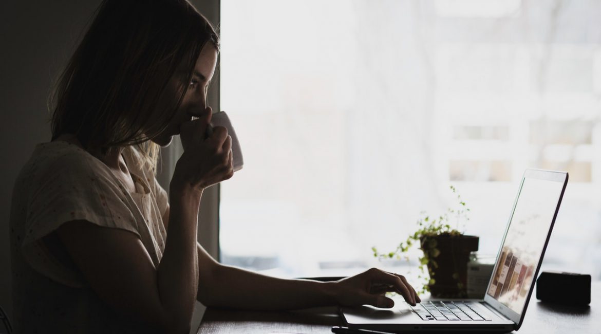 Kvinde sidder og drikker kaffe foran computer